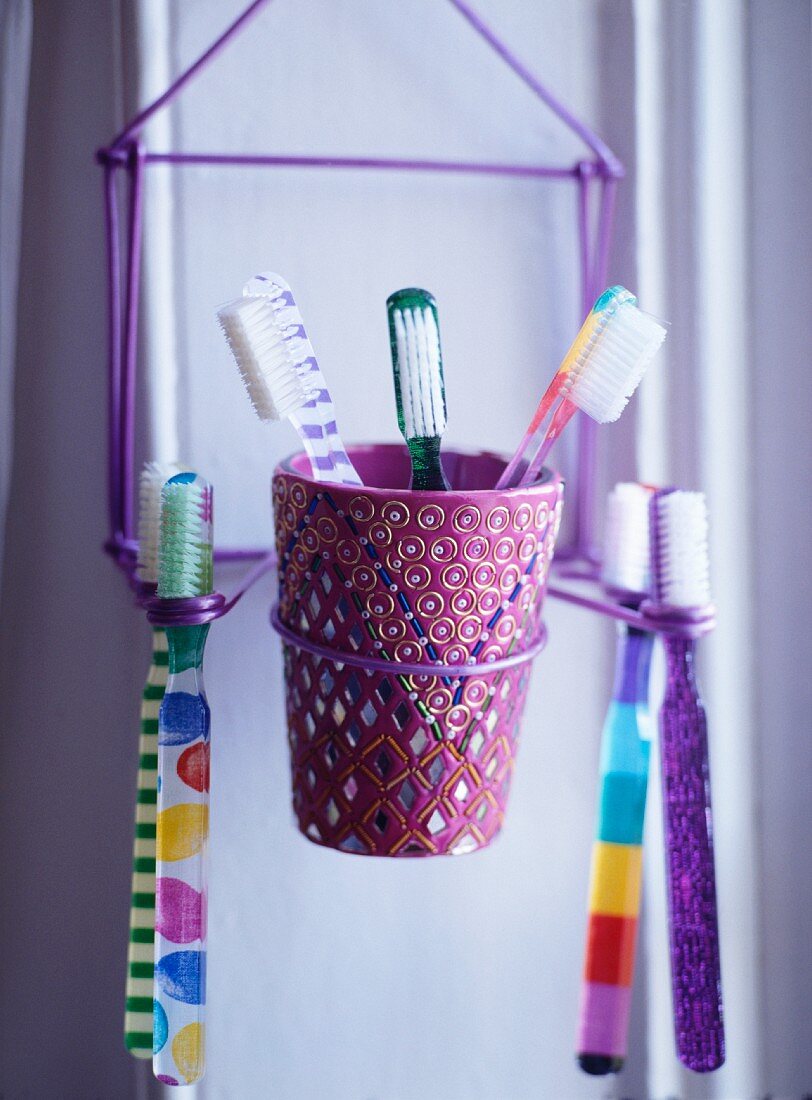 Gestell aus violettem Draht mit Zahnbürsten und verspieltem Zahnputzbecher