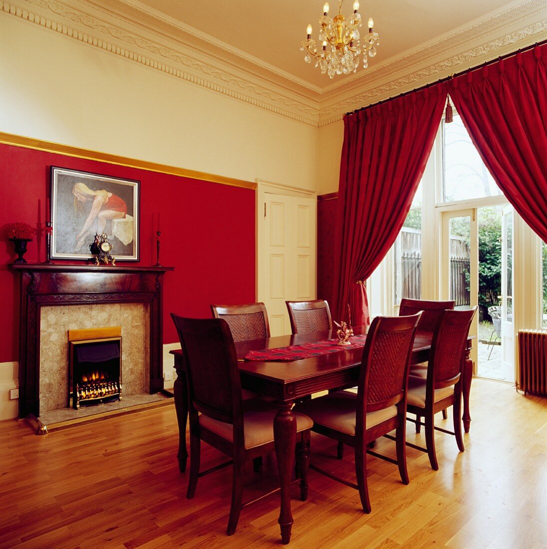 Elegantes Esszimmer mit rotbraunen Möbeln, rotem Theatervorhang und Kamin vor halbhoher roter Wand