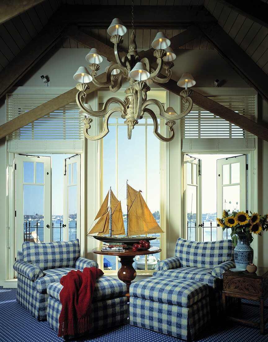 Sessel und Fussschemel mit blau kariertem Bezug und ein Modellboot in einem Wohnzimmer mit Blick auf das Meer