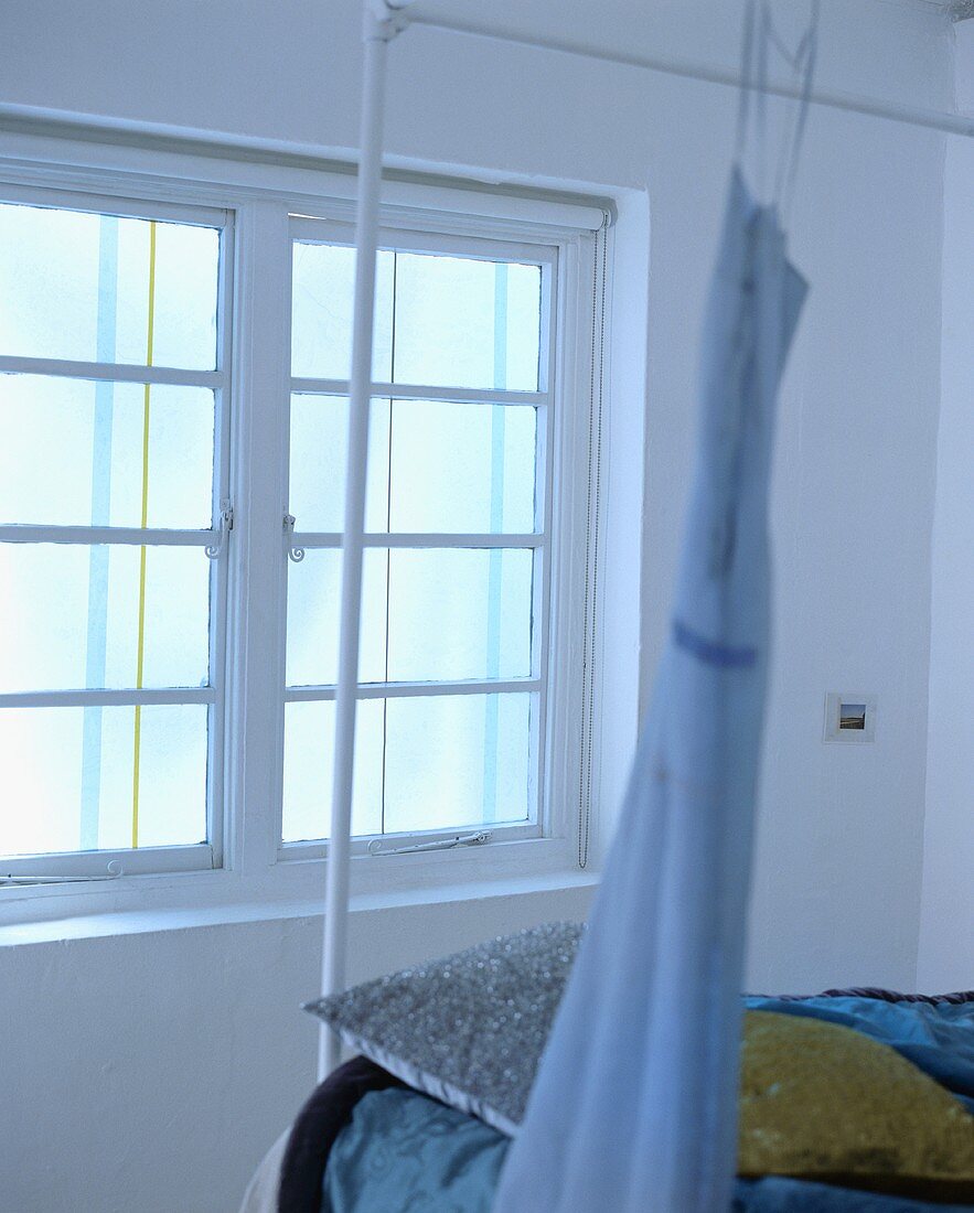 Blaues Kleid hängt auf dem weissen Metall-Bettgestell vor dem Fenster im Schlafzimmer