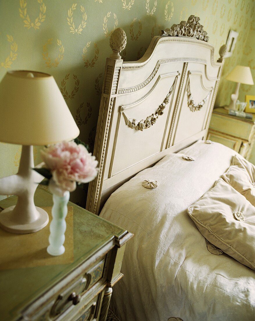 Ein Nachttisch neben einem cremefarbenen Bett in einem Schlafzimmer mit grün gold Tapete