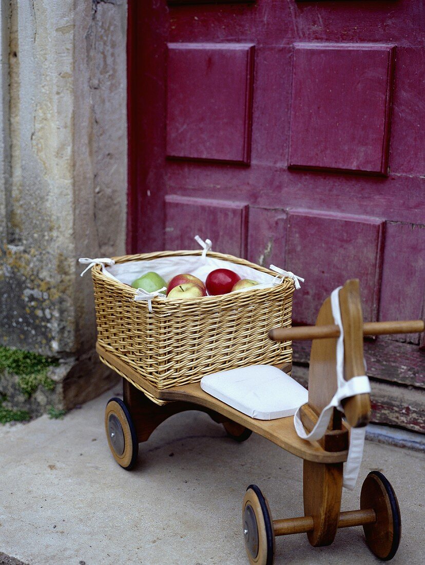 Ein Korb Äpfel auf einem Kinderdreirad aus Holz