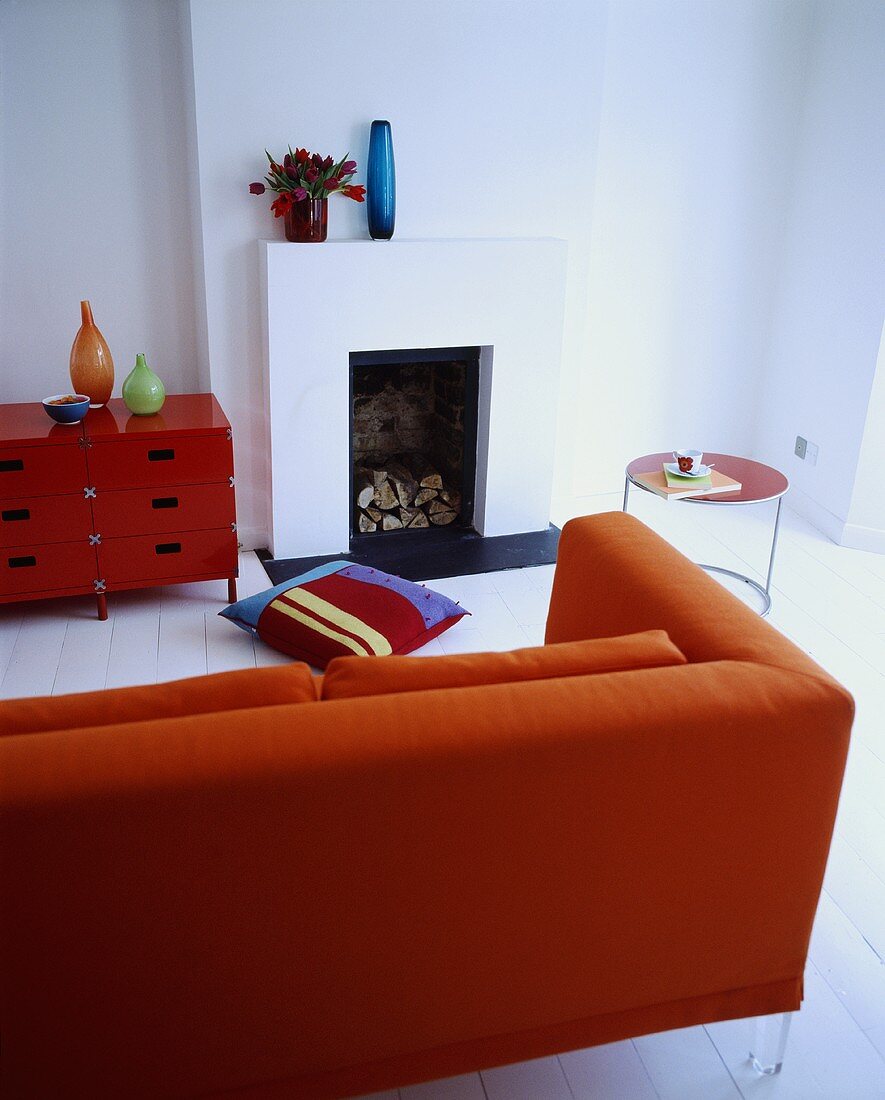 Rotes Sofa und Schränkchen in einem weissen Wohnzimmer mit Kamin