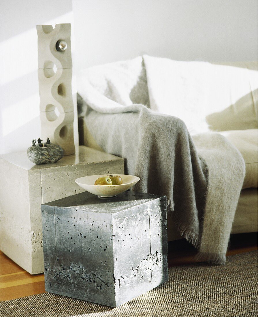 Skulptur und Würfel-Tisch aus Beton neben einem Sofa mit grauem Überwurf