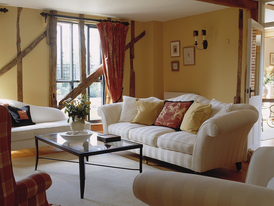 Wohnzimmer mit cremefarbenen Sofas und Fachwerk mit gelben Ausfachungen in umgebauter Scheune