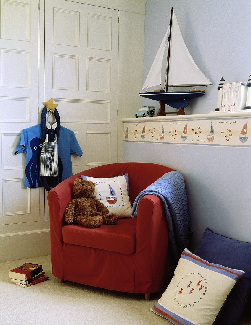 Kinderzimmer im maritimen Stil mit Segelboot auf gemauerter Ablage mit Segelboot-Bordüre und rotem Clubsessel mit Teddy
