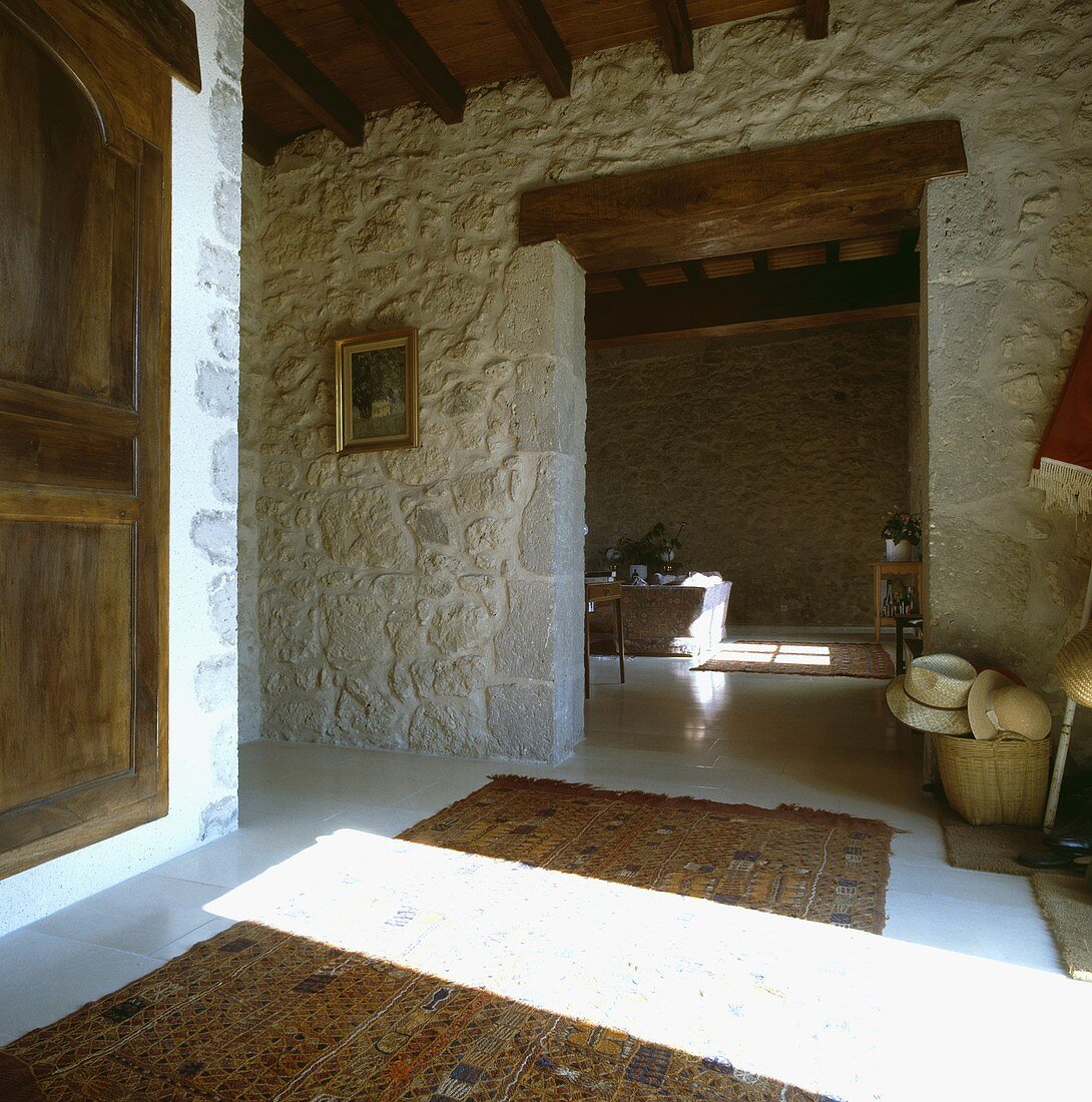 Raue Steinmauern und Holzdecke in großer, rustikaler Halle mit offenem Durchgang zum Wohnzimmer