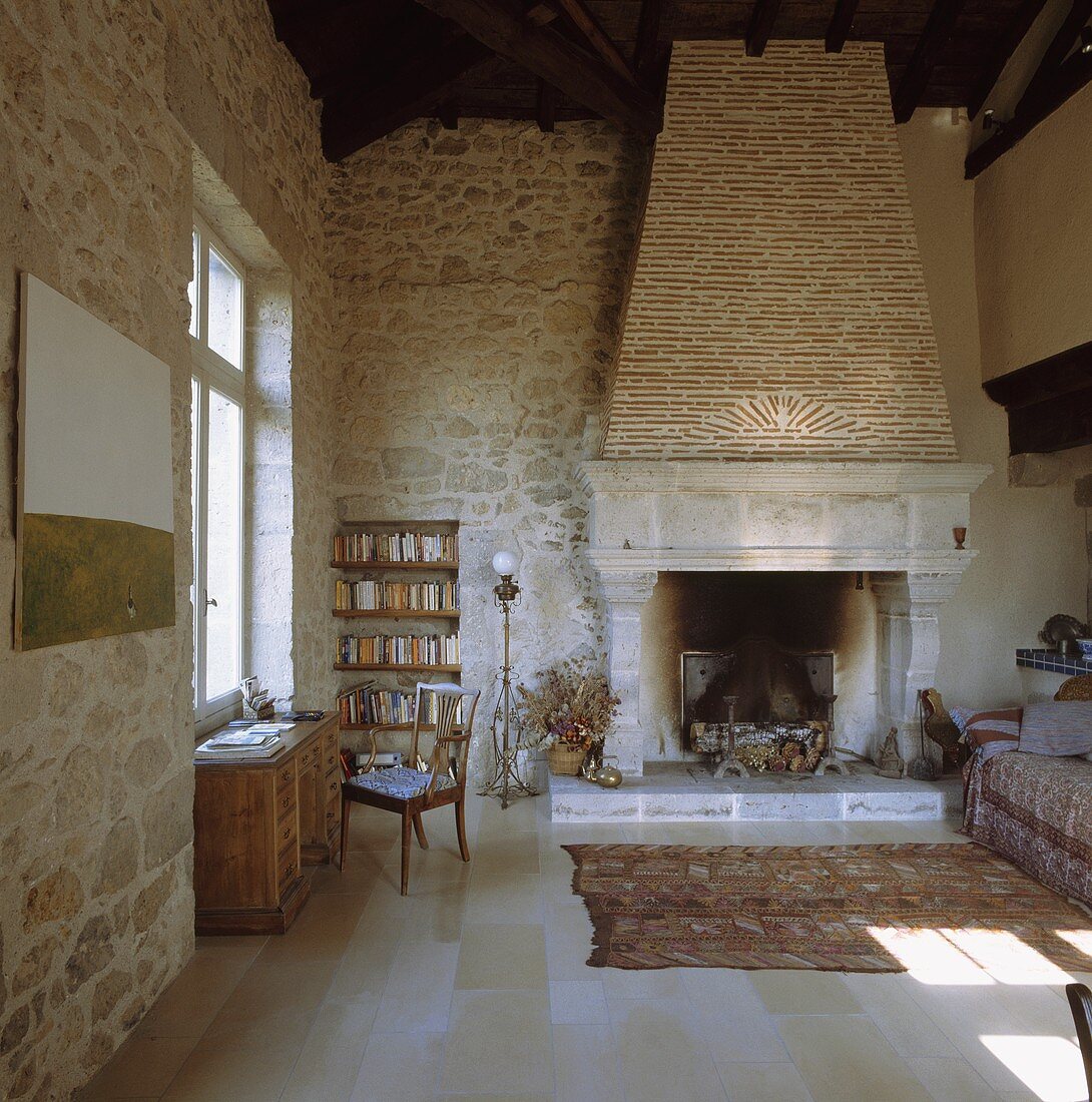Riesiges Wohnzimmer in französischem Haus aus dem 8. Jahrhundert mit eingebautem Regal in Natursteinwänden und Webteppich vor großem Kamin