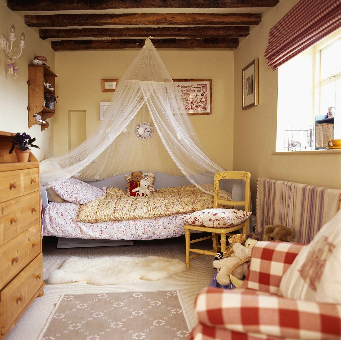 Moskitonetz über Bett mit dekorierten Teddys in Kinderzimmer mit Holzbalkendecke und rot-weiss-karierter Stoffjalousie