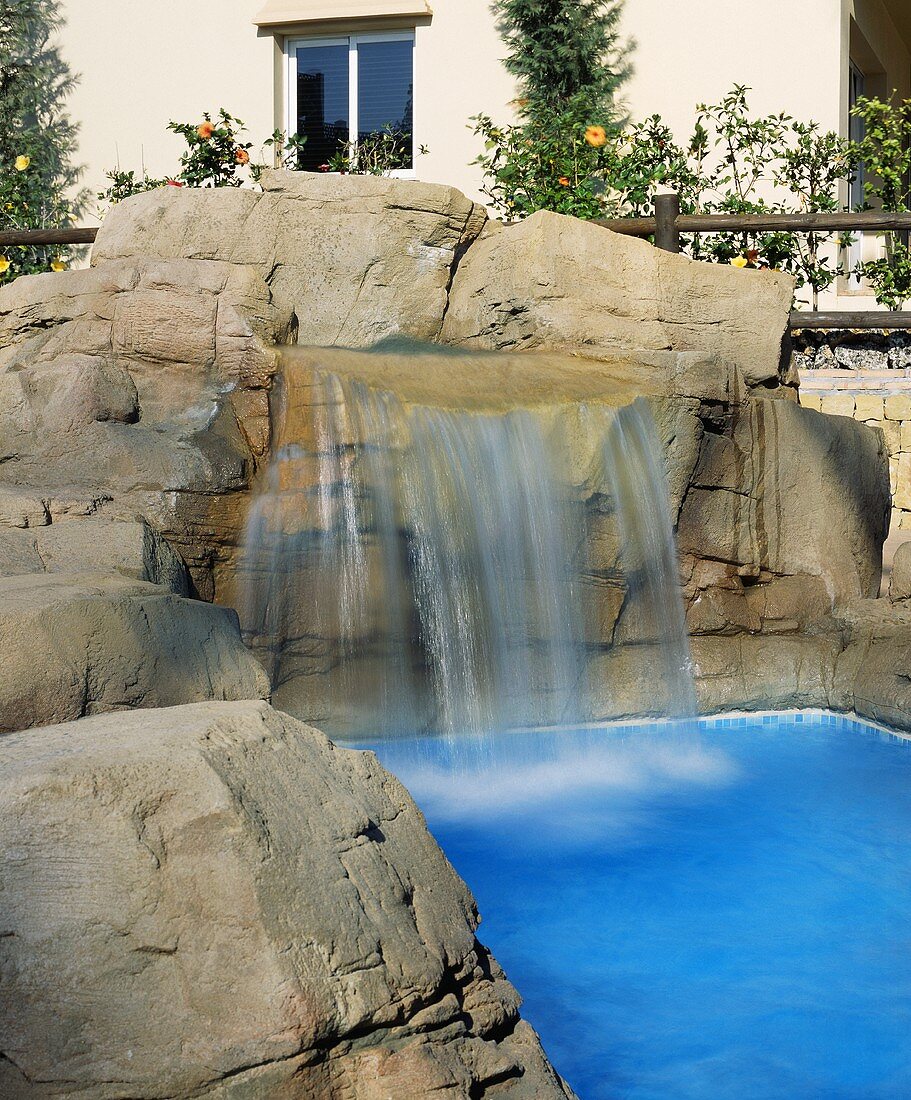 Schwimmbad mit natürlichen Felsen und Wasserfall vor einer spanischen Villa
