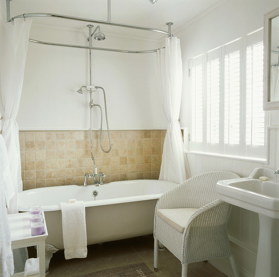 Landhaus-Badezimmer mit weißem englischen Korbstuhl neben Badewanne mit Klauenfüssen und Vorhang an ovaler Brausestange