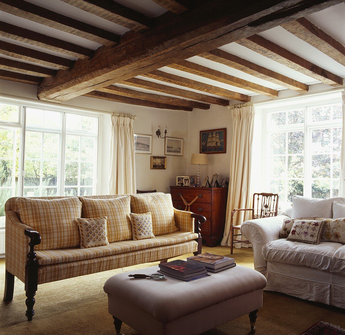 Wohnzimmer in altem Landhaus mit niedriger Holzbalkendecke über antikem Sofa
