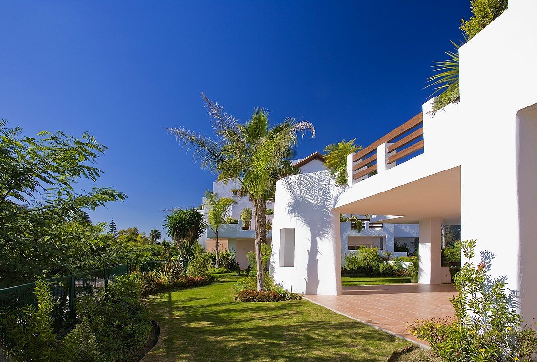 Garten mit Palmen und Rasen vor einer modernen weissen spanischen Villa mit Balkon