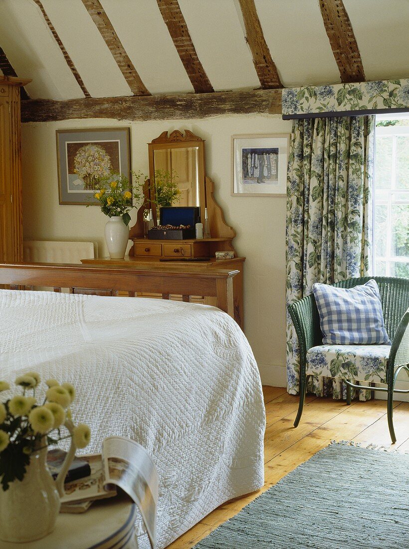 Lloyd-Loom-Stuhl mit Kissen in einem ländlichen Schlafzimmermit gemusterten Gardinen