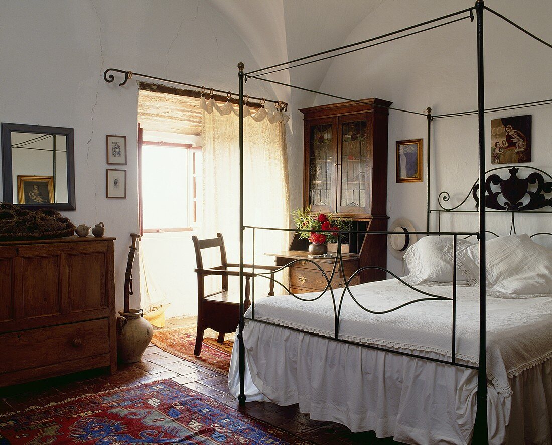 Ein einfaches Himmelbett mit Metallgestell in einem ländlichen weissen Schlafzimmer