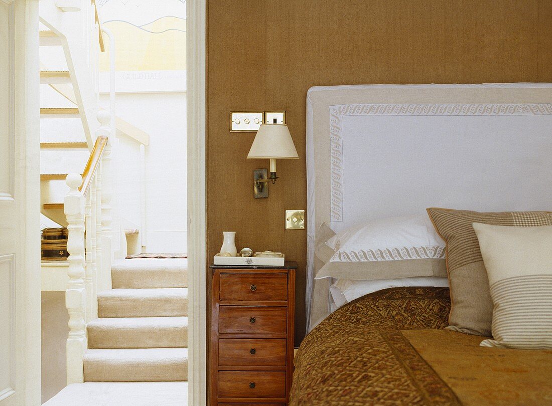Creme- und Weißfarbene Kissen und Bettwäsche mit passendem Kopfteil über dem Bett neben offener Tür zur Treppe