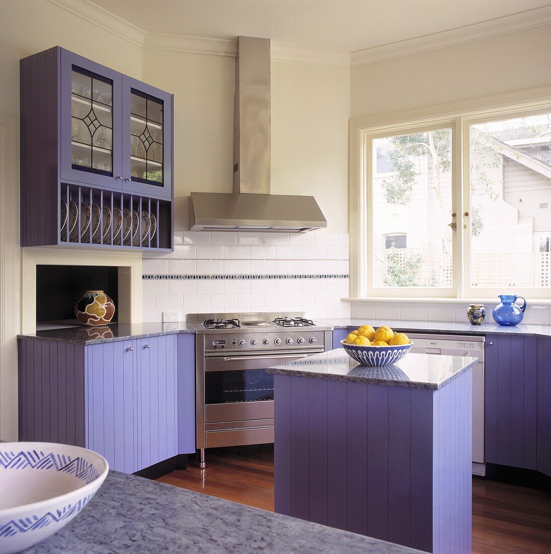 Eine kleine Küche mit modernen Arbeitsgeräten und violetten Schränken, die zu den gelben Zitronen kontrastieren