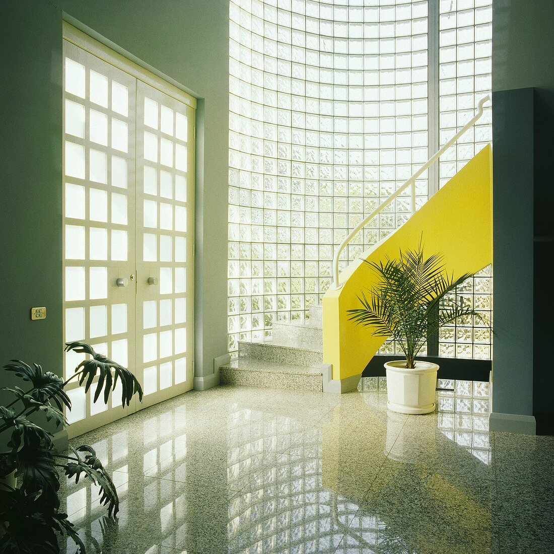 Eine bogenförmige Glassteinmauer und eine gelbe Treppe dominieren eine moderne Halle mit einem polierten Fußboden hellgrau und doppelt verglaste Türen