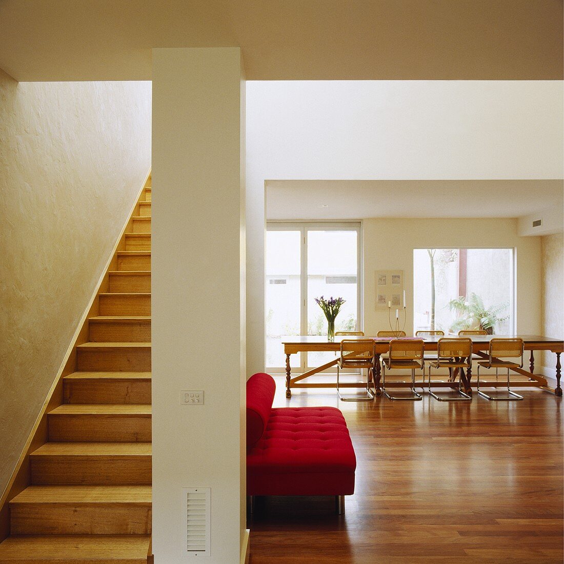 Eine Holztreppe führt von dem modernen Wohnbereich mit Parkettboden und einem roten Sofa in den oberen Etagen