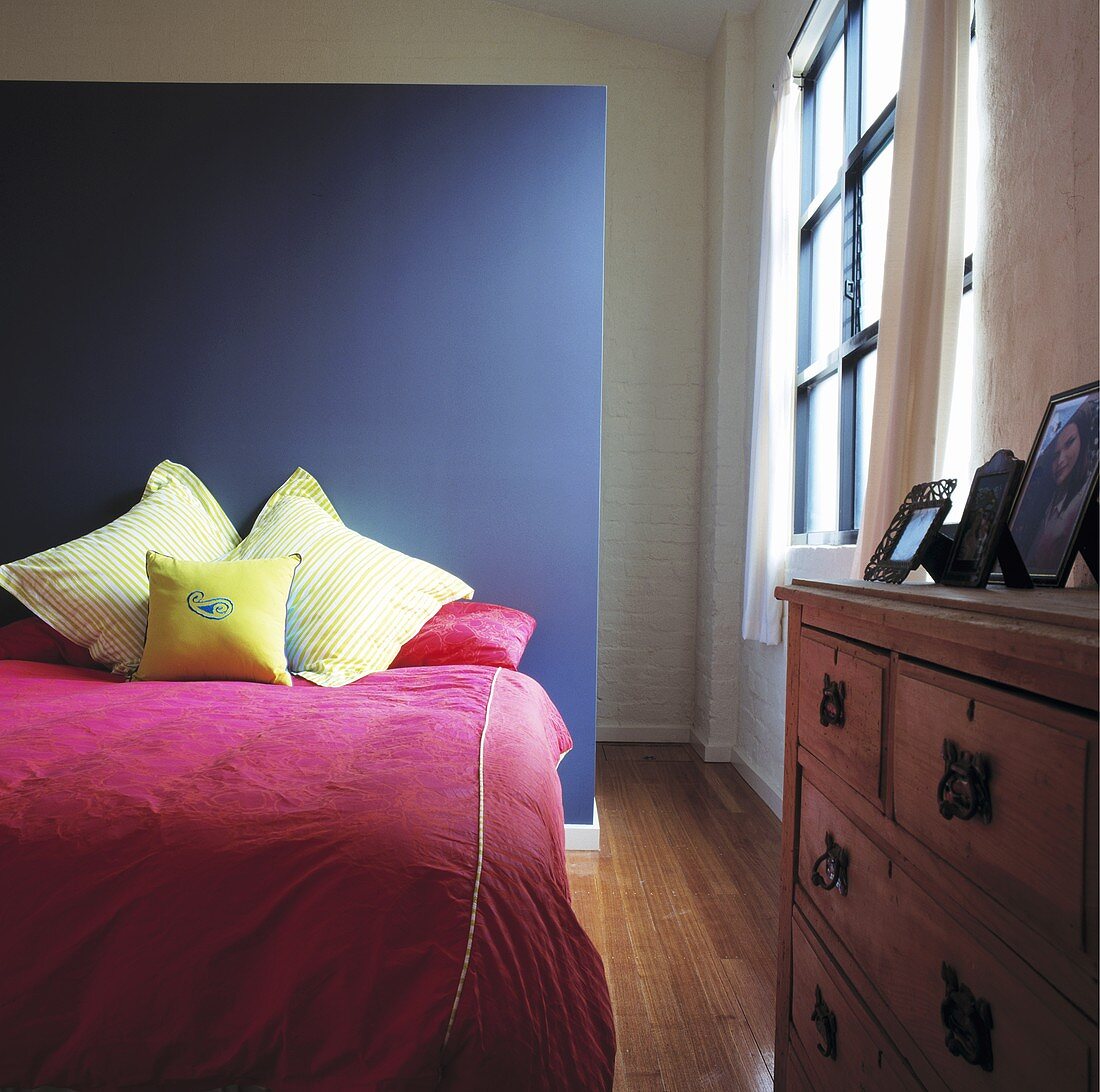 Ein Bett mit rosa Bettwäsche ist vor einer grauen Wand platziert worden, die gleichzeitig eine Trennwand darstellt