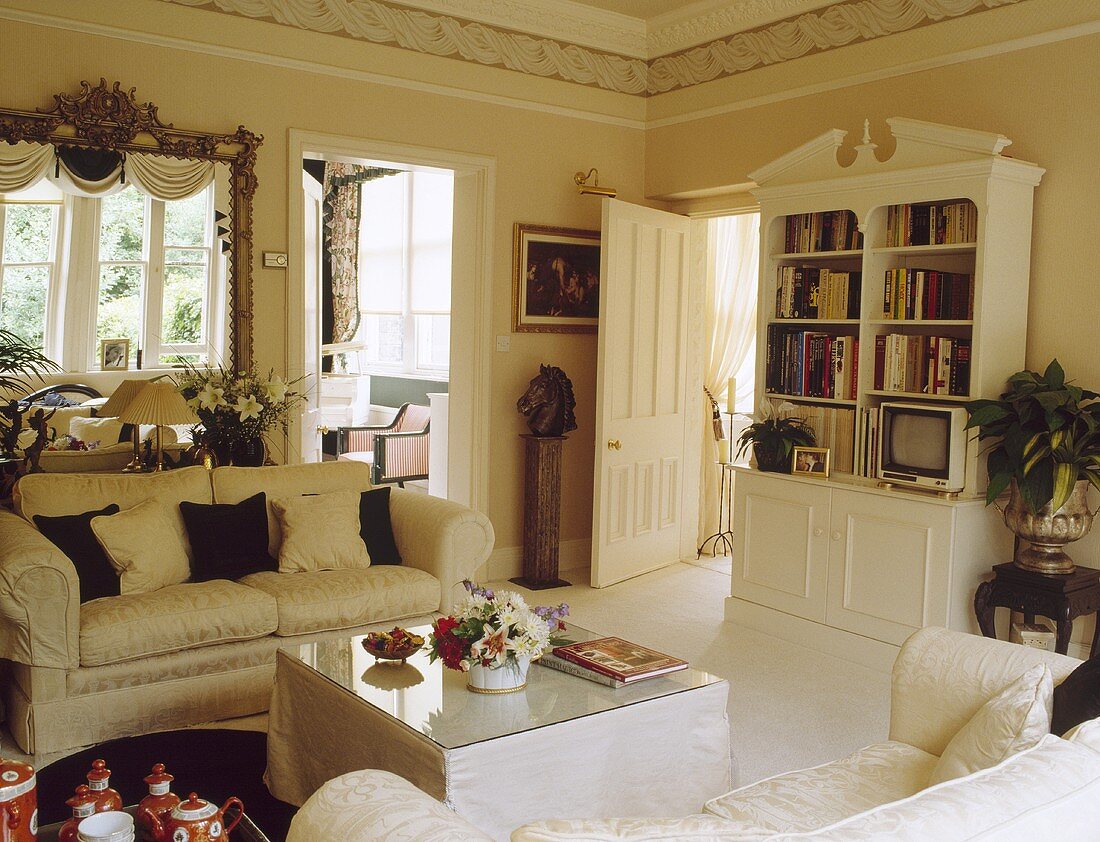 Cremefarbiges Sofa und ein Bücherregal richten ein traditionelles und schlichtes Wohnzimmer ein