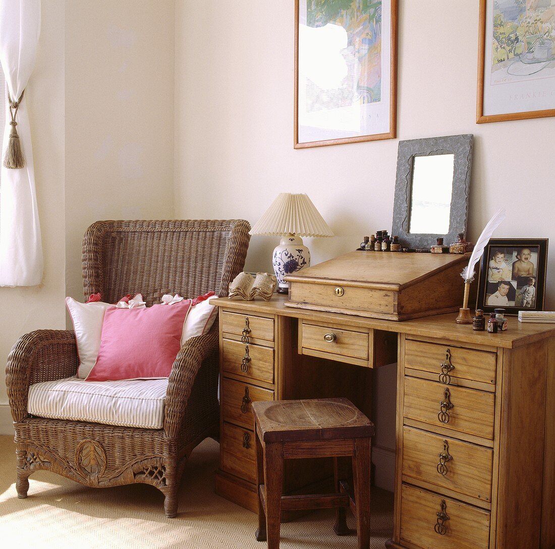 Pinke und weiße Kissen liegen auf einen Korbsessel, der neben einen alten Kiefer-Schreibtisch steht