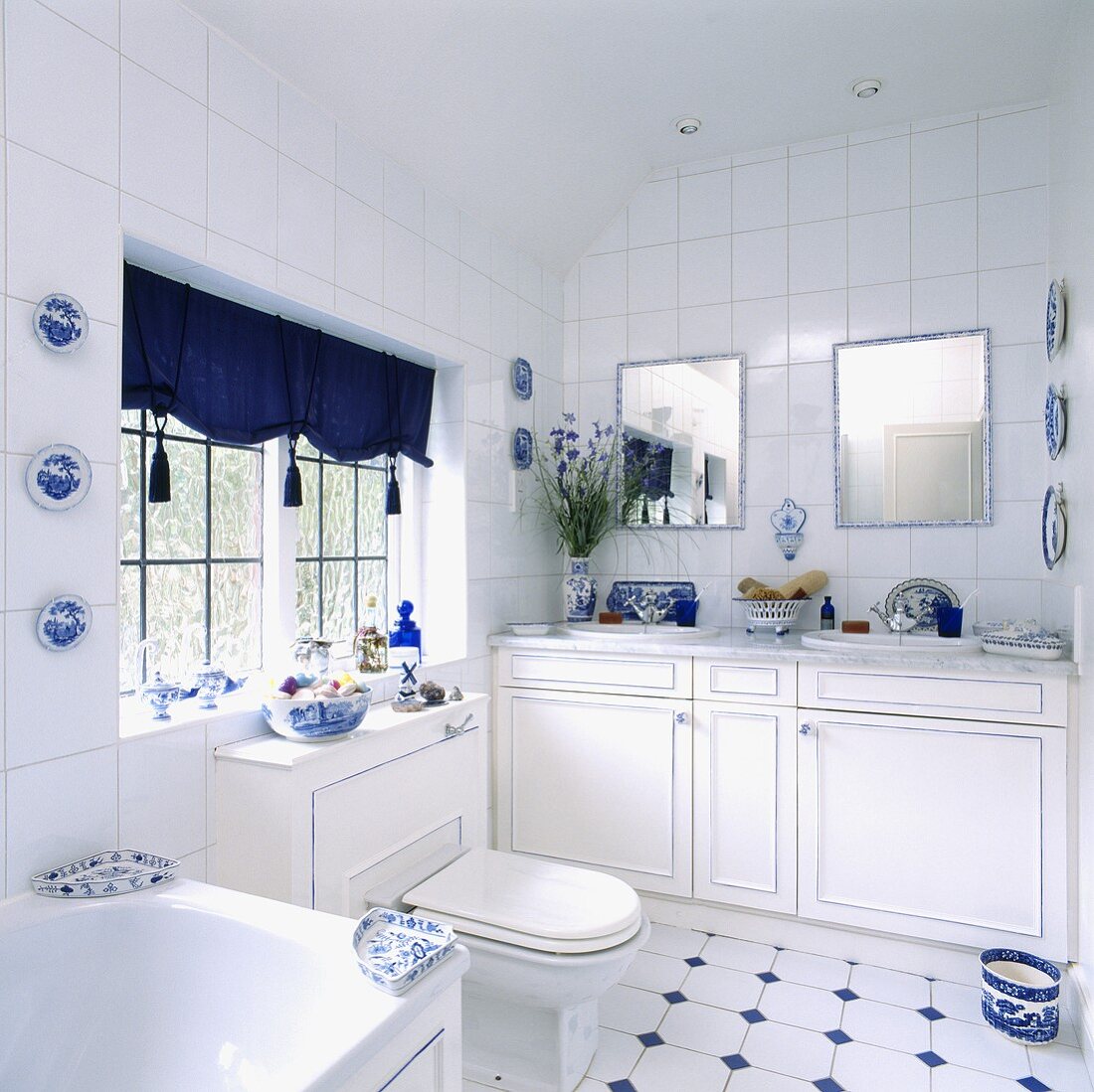 Zwei Waschbecken mit jeweils einen kleinen Spiegel darüber richten das weiße Badezimmer ein, das durch blaue Farbakzente aufgepeppt wird