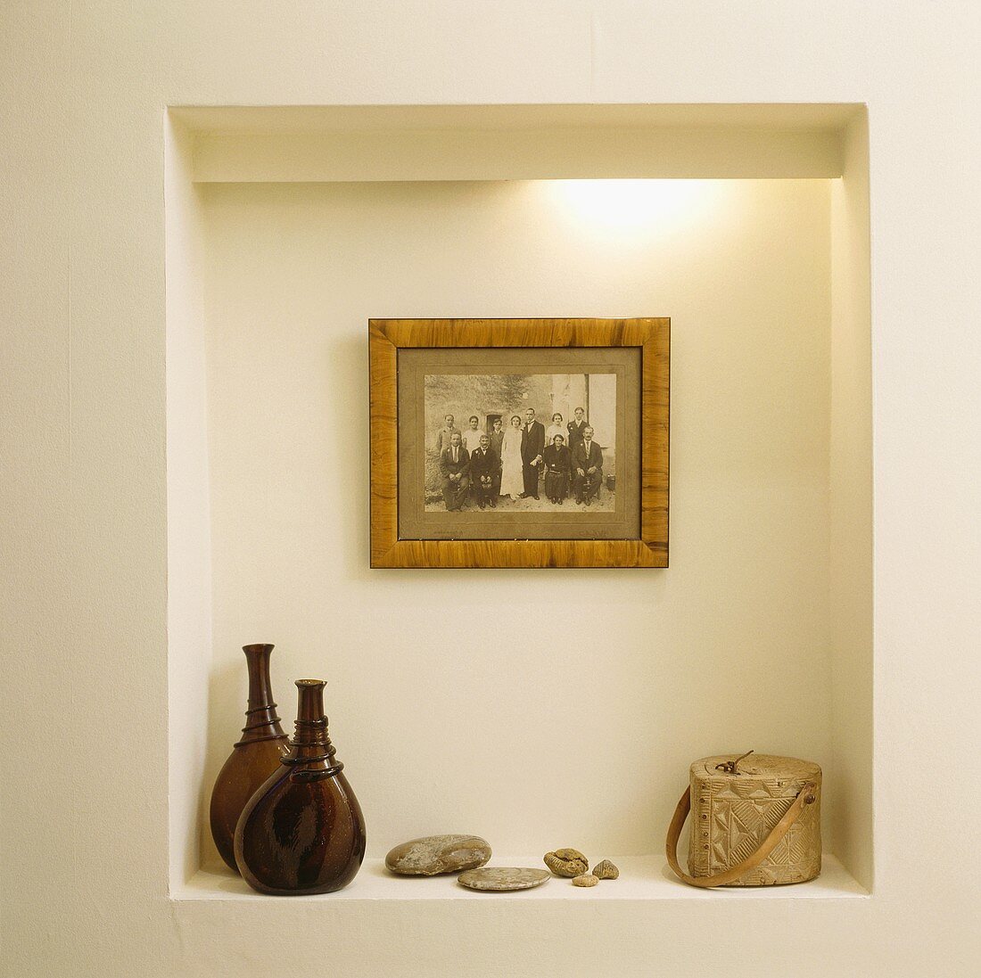 Ein altes schwarz-weiß Foto hängt in einer beleuchteten Nische, auf der zwei braune Glasflaschen und ein Specksteinbehälter stehen