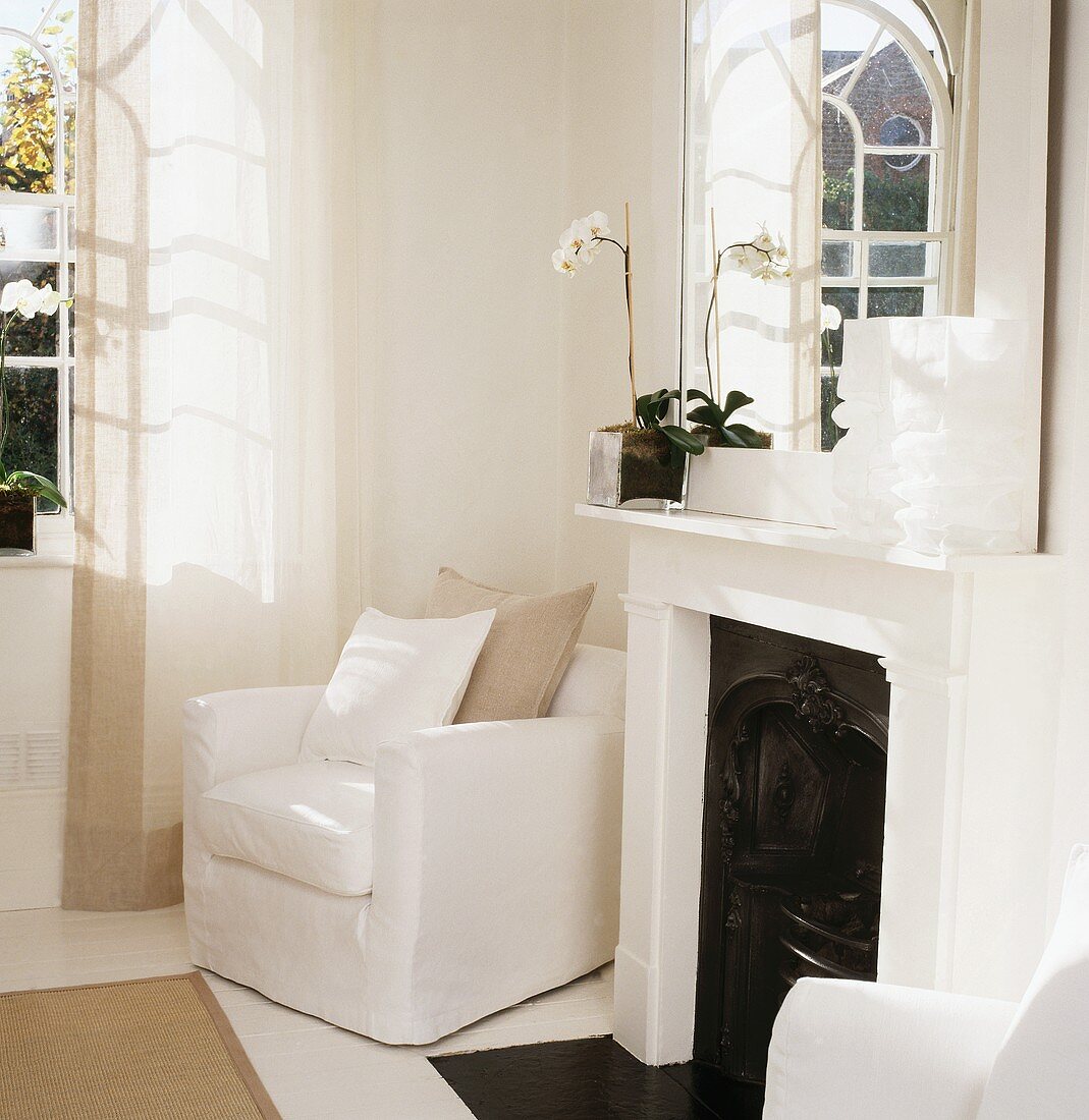 Ecke in weißem Landhaus-Wohnzimmer mit Sesseln, Kamin, Spiegel und Sonnenschein