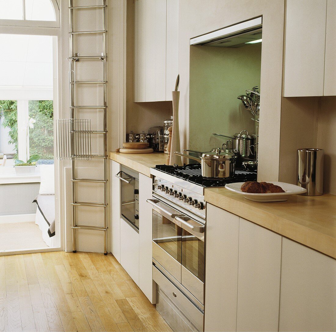 Helle, schlicht-moderne Einbauküche mit hoher Stahlleiter neben Durchgang zum abgesenkten Wohnraum
