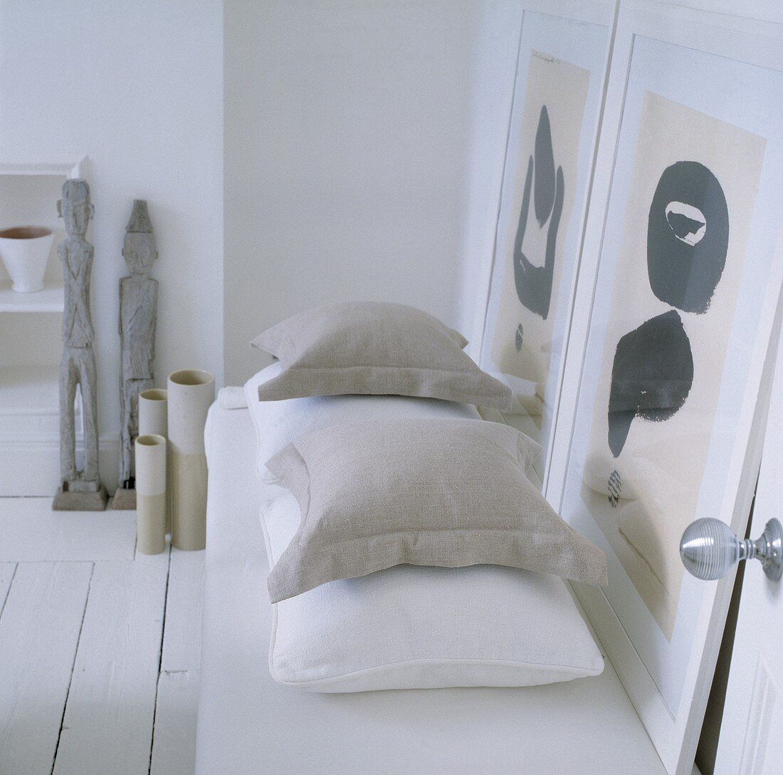 Kissen und zwei moderne Gemälde auf einer Liege mit Skulpturen und Vasen daneben als grau / beige Farbklänge in weißem Raum
