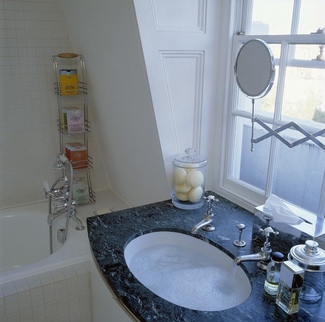 Schwarzer Marmorwaschtisch mit gefülltem Unterbaubecken und altmodischen Armaturen vor Sprossenfenster in weißem Bad