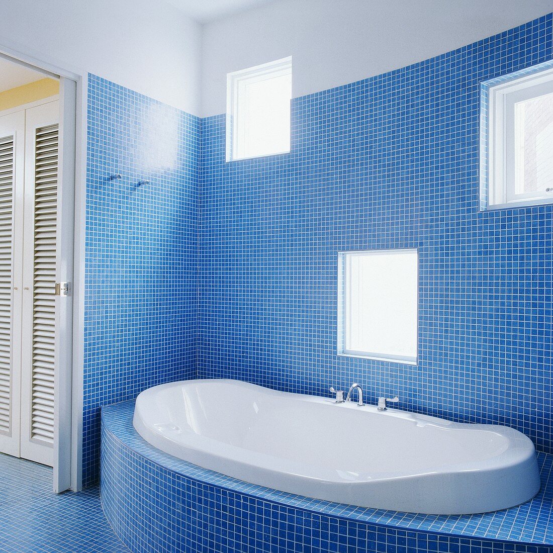 Ein modernes und mit blauer Mosaik gefliestes Badezimmer und eine weiße Badewanne