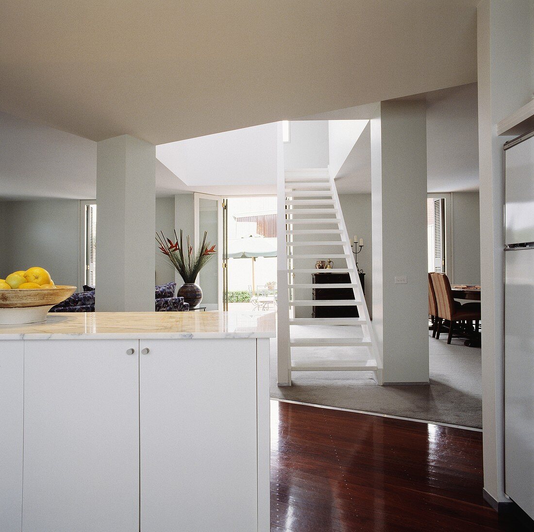 Weisser Küchenunterschrank mit Marmorplatte in modernem offenen Wohnraum mit offener weisser Holztreppe und glänzendem Holzparkett