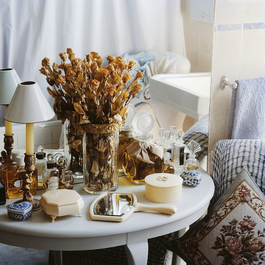 Getrocknete Rosen in einer Vase auf weißem Tischchen mit Sammlung von Elfenbeindosen und Parfümflaschen vor Spiegel in Badezimmer