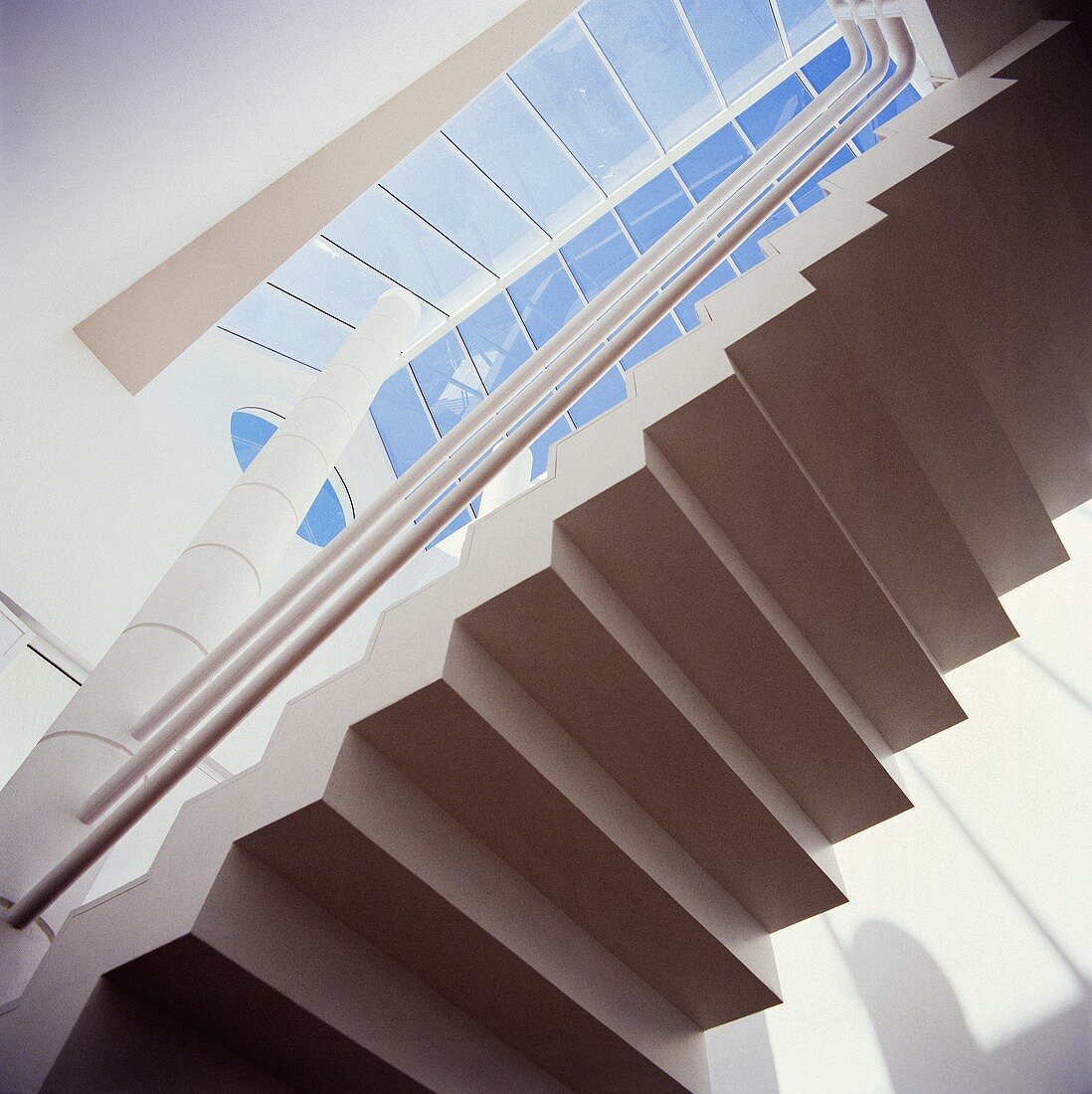 Blick von unten auf eine weiße, moderne Steintreppe in Halle mit Glasdach