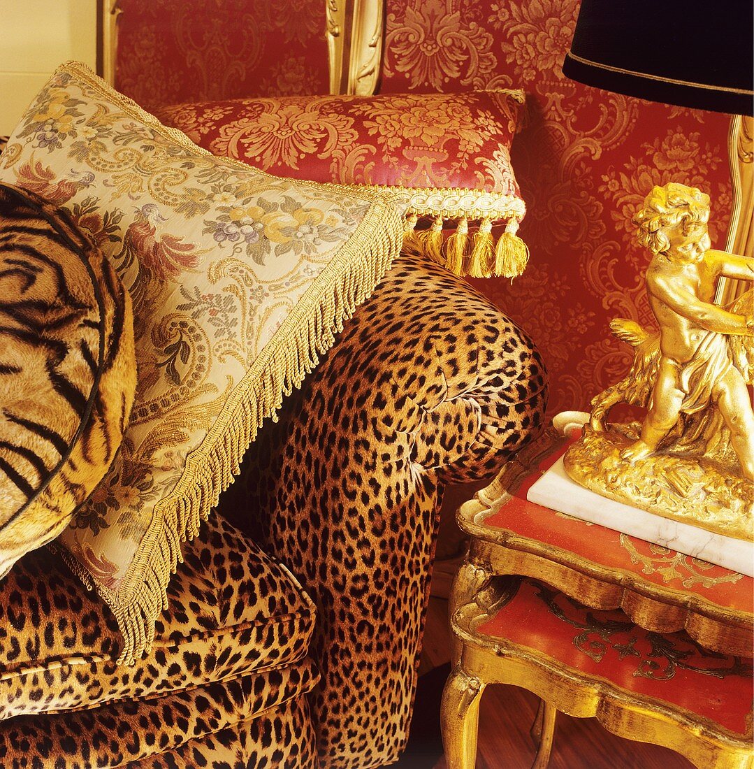 Nahaufnahme von Seidenkissen auf Sofa mit Animalprint neben vergoldeter Figur als Lampenfuss