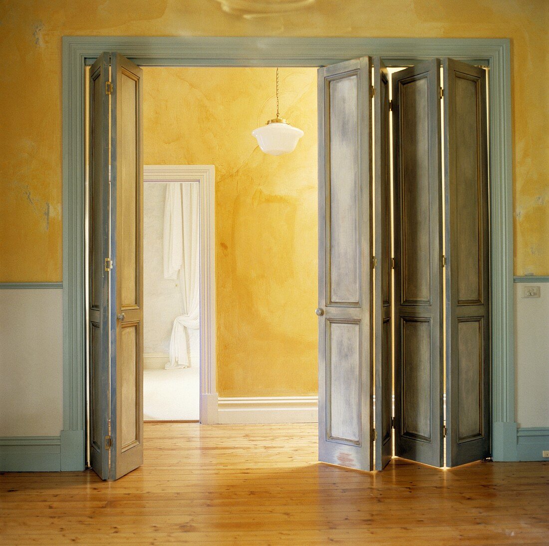 Graublaue Falt-Kassettentüren in gelbem Wohnraum mit Holzboden und Blick auf Korridor