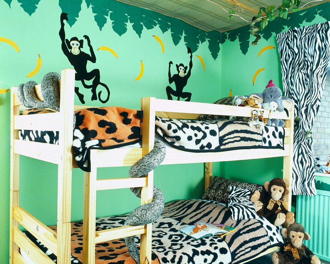Bettwäsche mit Tierfell-Motiv und Kuscheltiere auf hölzernem Etagenbett in Kinderzimmer mit grünem Dschungel-Wandbild