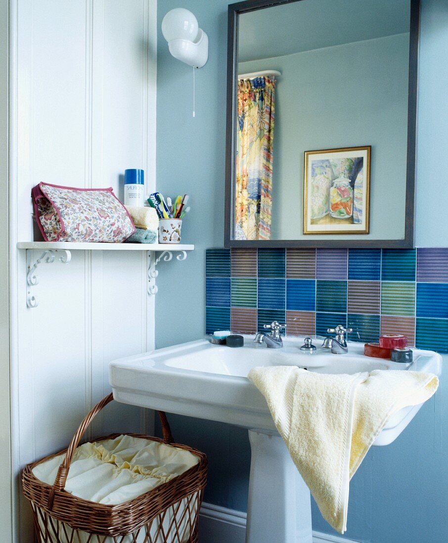 Spiegel und mehrfarbige Fliesen über weißem Säulen-Waschbecken und seitlichem Bord mit verschnörkelter Wandhalterung