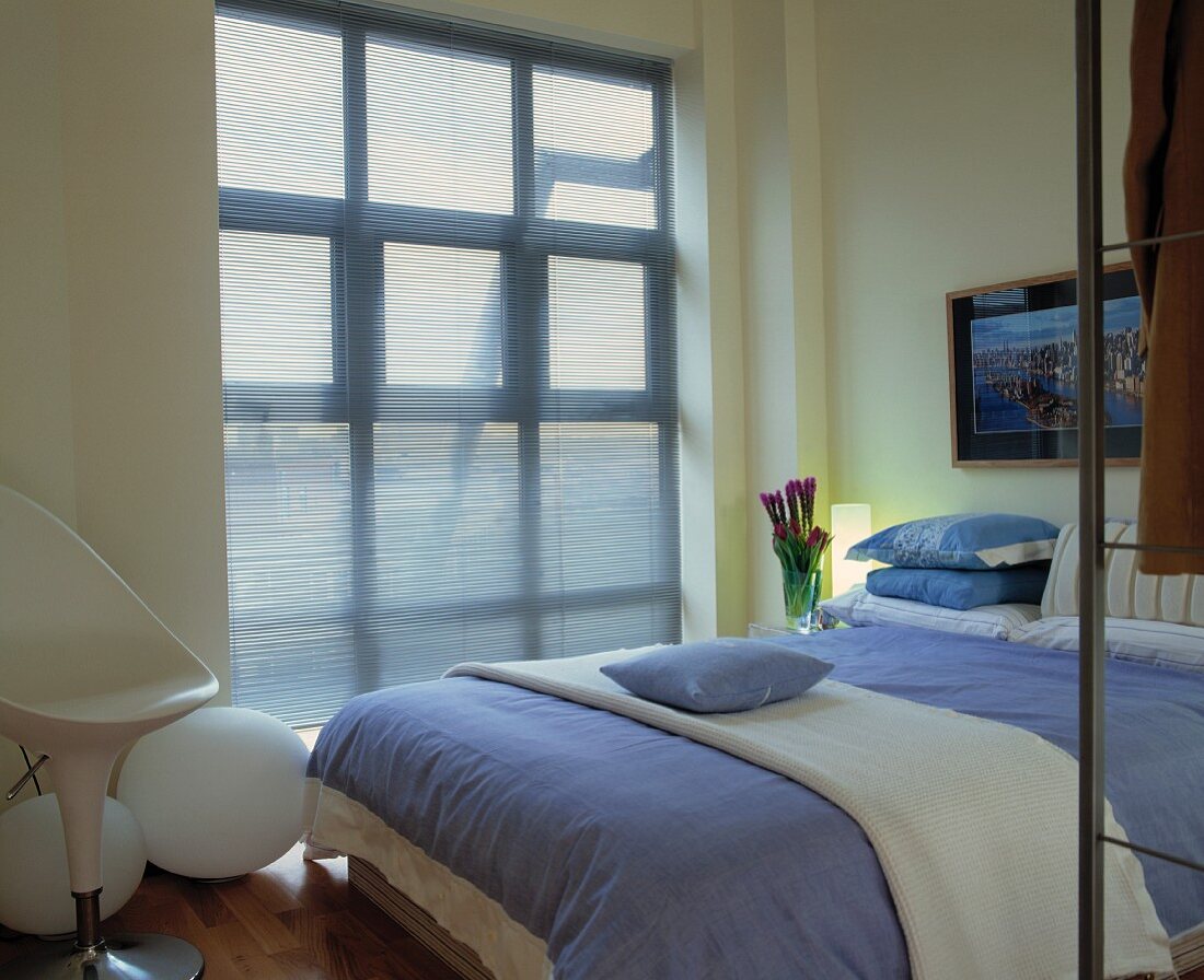 Von durchsichtigem, blauem Stoff verhangenes Fenster in modernem Schlafzimmer mit Bettzeug in Hellblau und Weiß