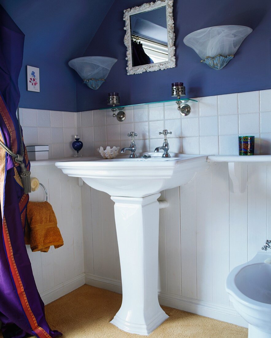 Säulenwaschbecken vor weiss-blauer Wand mit Spiegel und Lampenpaar in traditionellem Badezimmer