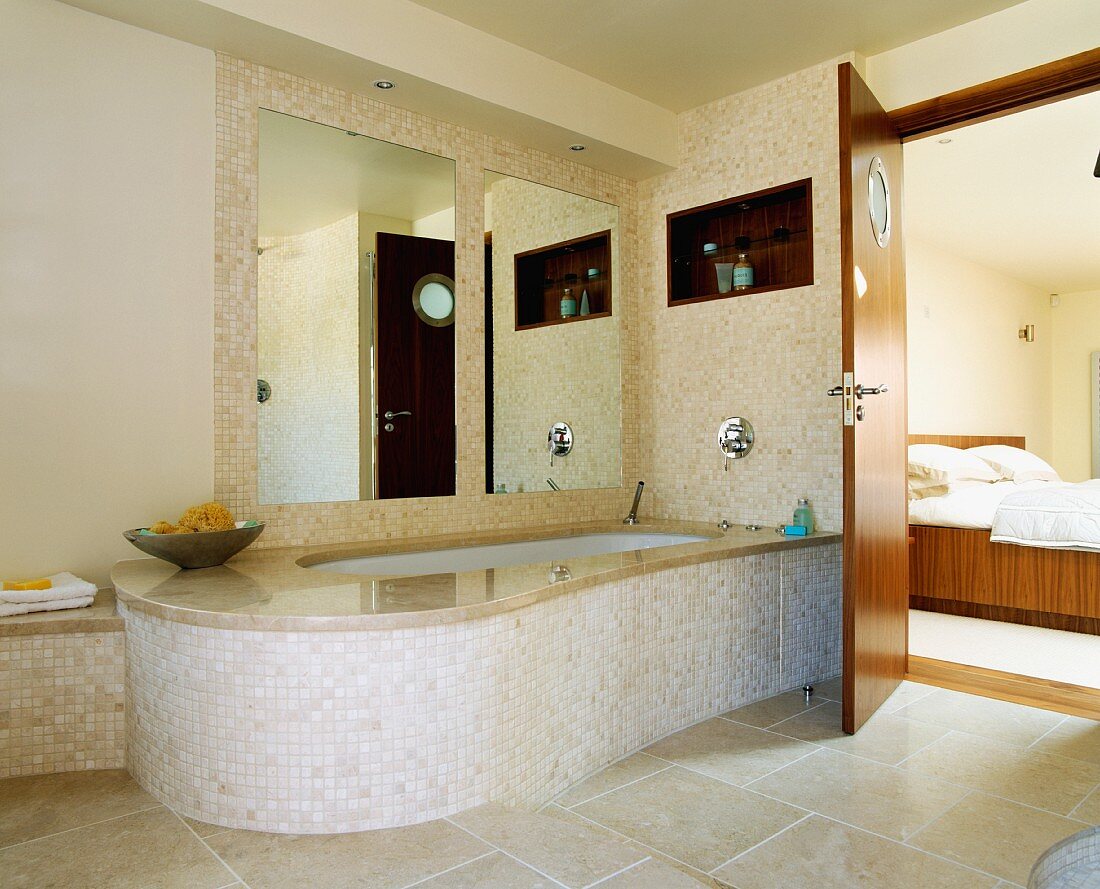 Grosse Spiegel hinter Badewanne mit breiter Marmorumrandung und Mosaikfliesen in beigem Bad ensuite