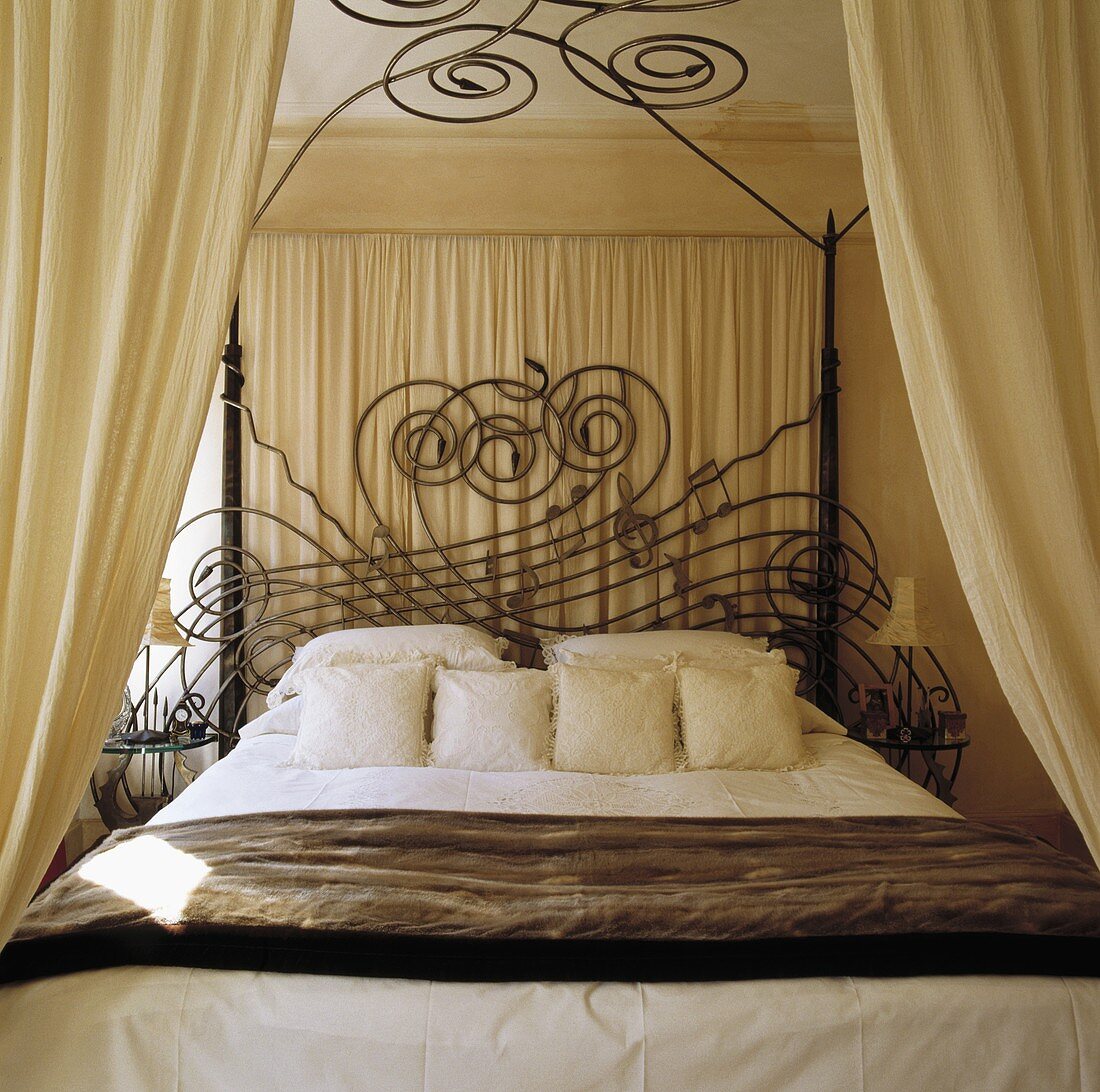 Ein schmiedeeisernes Bett von Mark Brazier-Jones mit cremefarbenen Kissen und Vorhängen in einem cremefarbenen Schlafzimmer