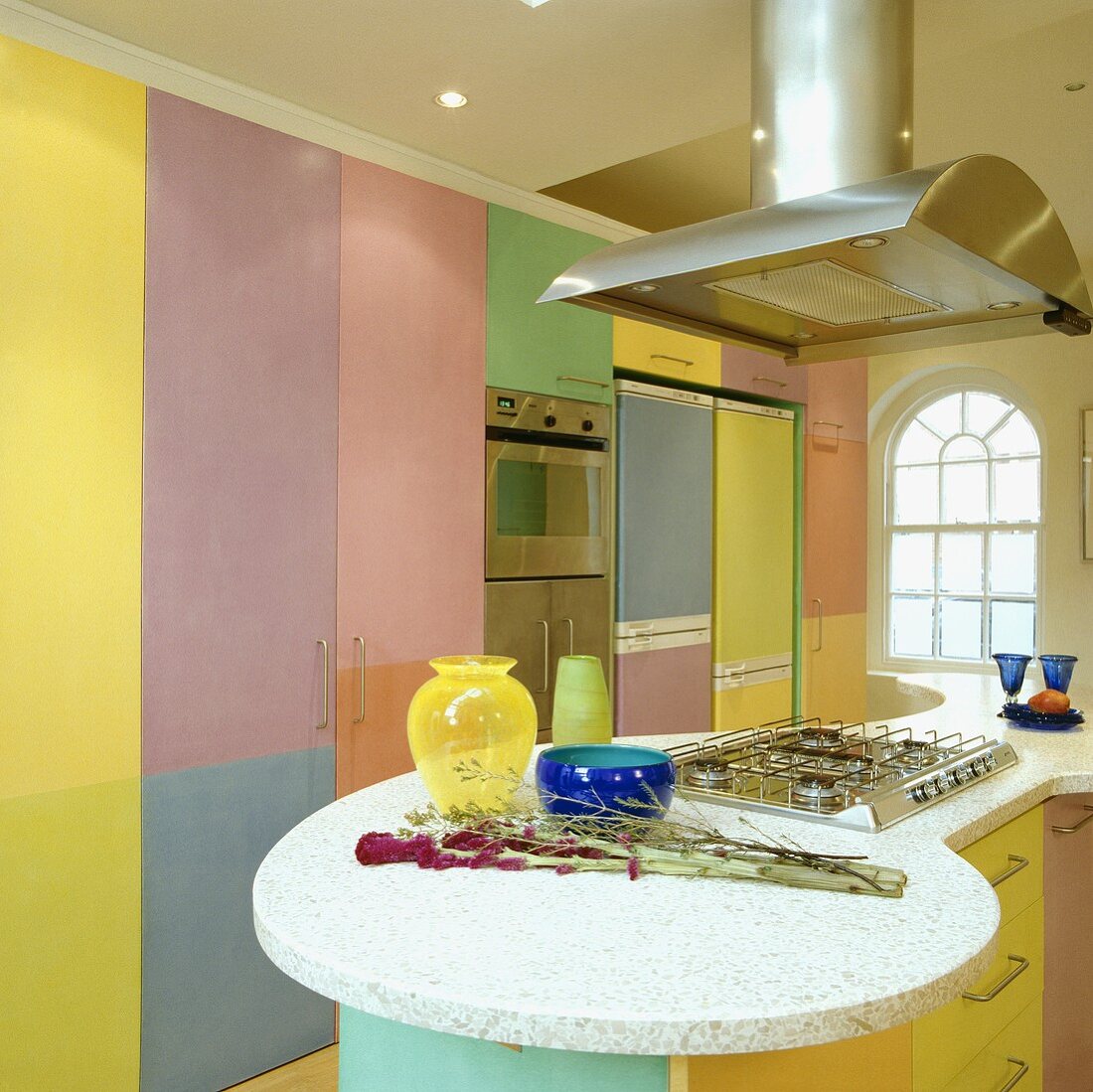 Edelstahl-Dunstabzug über einem Gasherd auf einem Halbinselelement mit Marmorplatte in einer bunten pastellfarbenen Küche