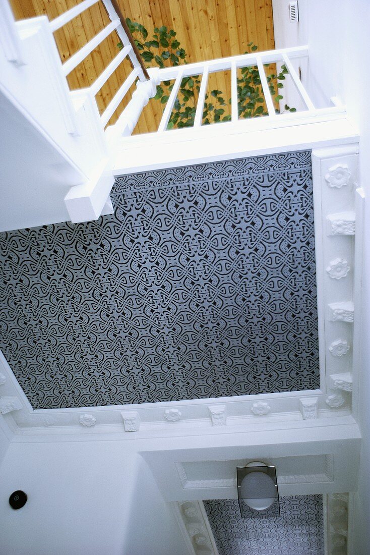 Blick von unten auf eine grau und weiss gemusterte Decke und auf ein Treppengeländer
