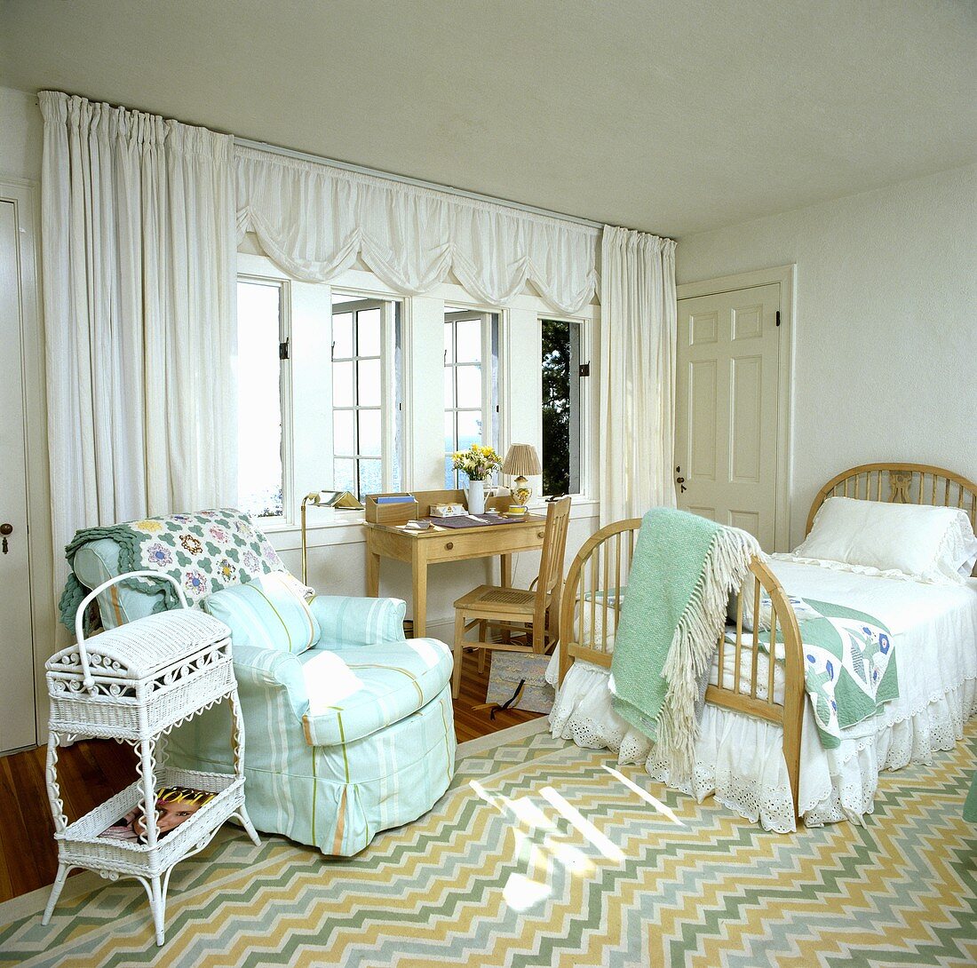Schlafzimmer mit Küstenaussicht mit weißen Vorhängen, gestreiftem, türkisen Sessel, Holzbett und einem Teppich mit Zick-Zack-Muster