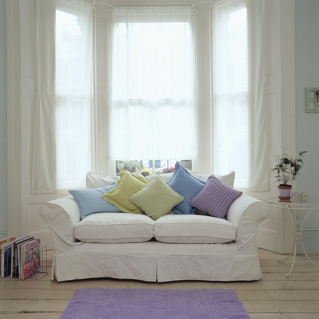 Pastellfarbene Kissen auf einem weissen Sofa vor dem Erkerfenster in einem Wohnzimmer