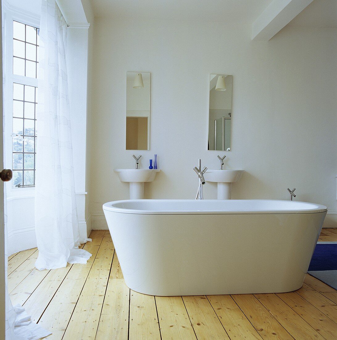 Eine frei stehende weiße Badewanne in einem Badezimmer mit Kieferboden