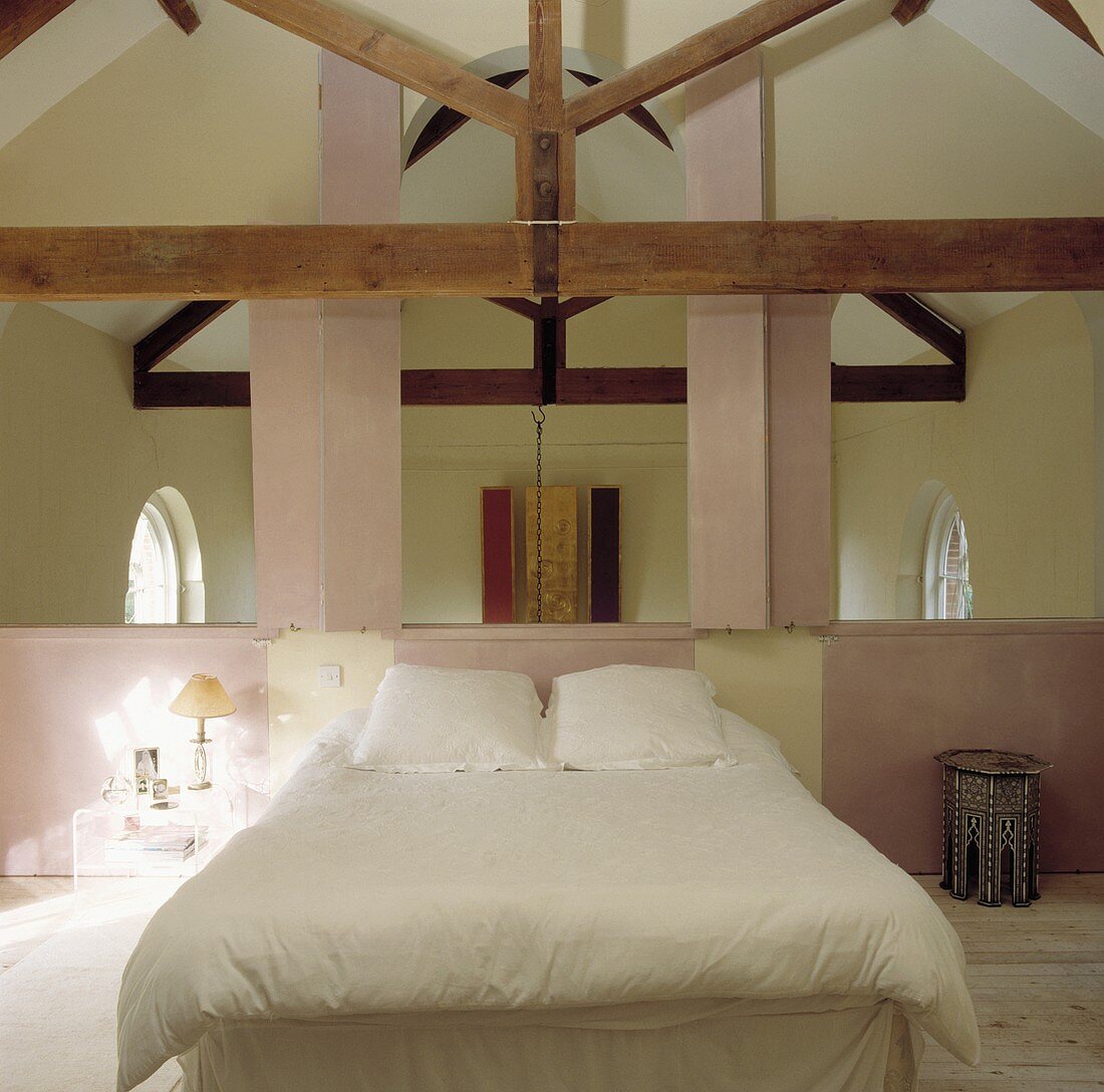 Bett mit weißen Kissen und Decke in einem Mezzanine-Schlafzimmer mit Balken und rosa Wänden